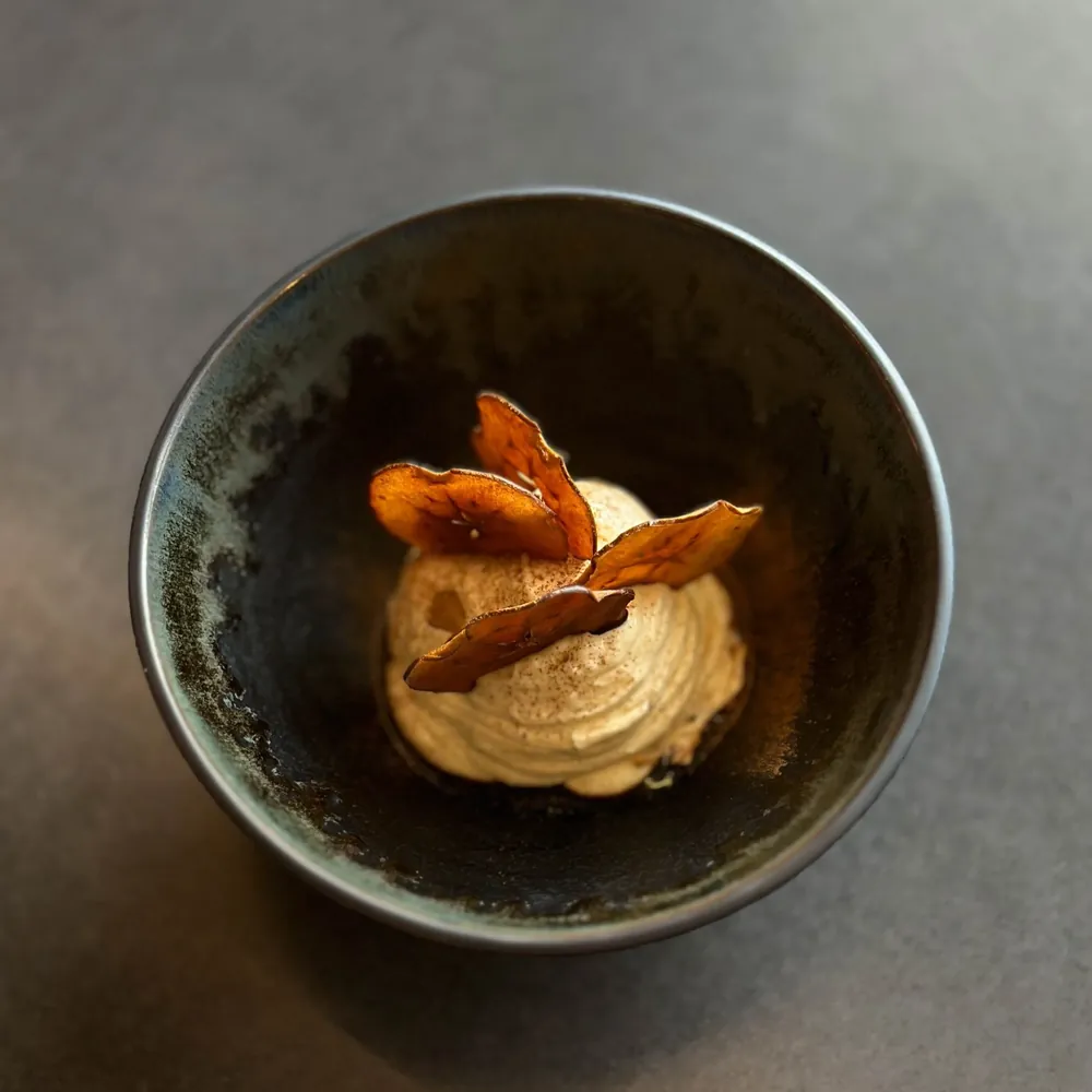 A dessert with a swirl of cream topped with nut slices in a black cup on a gray surface.